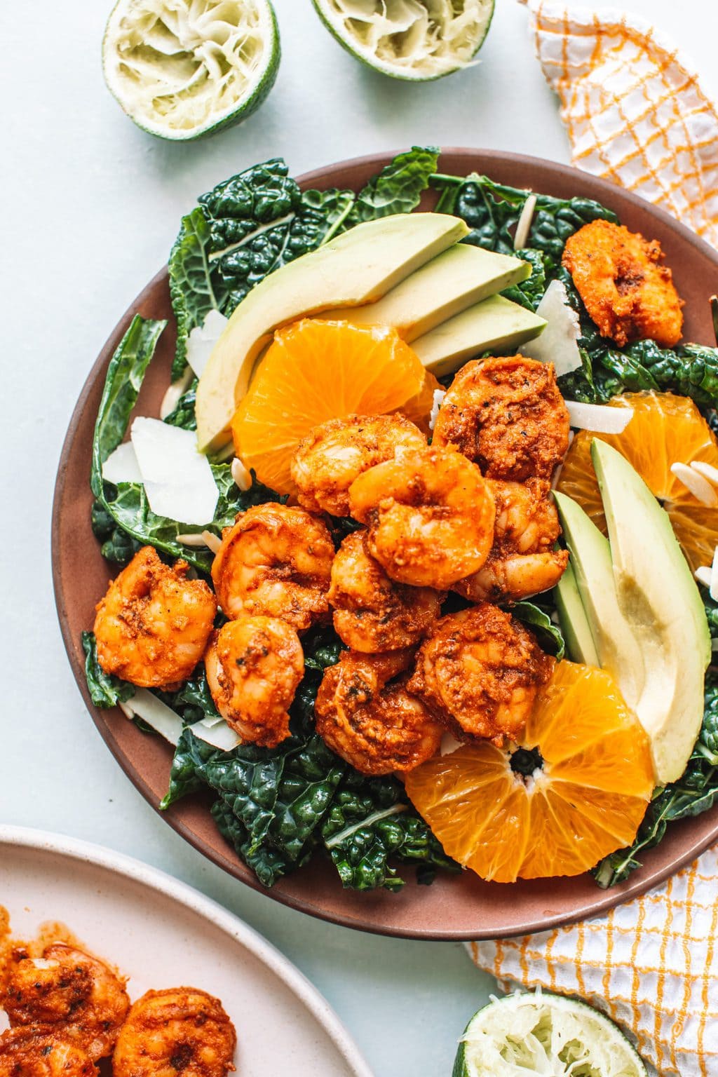 Blackened shrimp on bed of lettuce with avocados and orange slices on red plate.