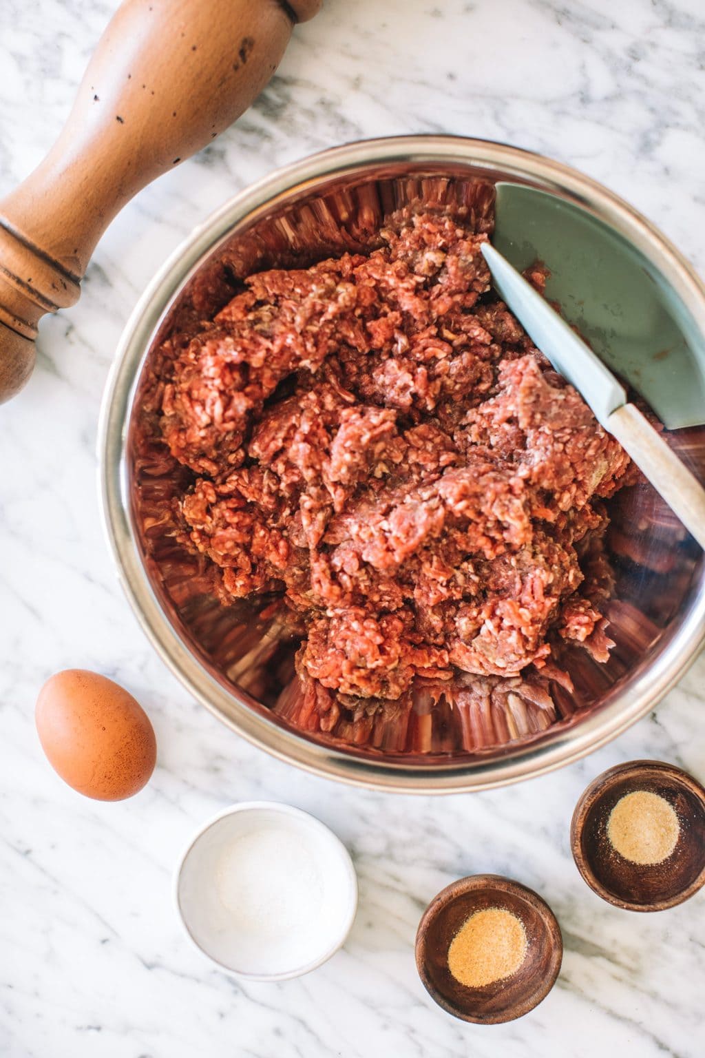 A prep bowl with ground beef, an egg, kosher salt, garlic powder, onion powder and pepper.