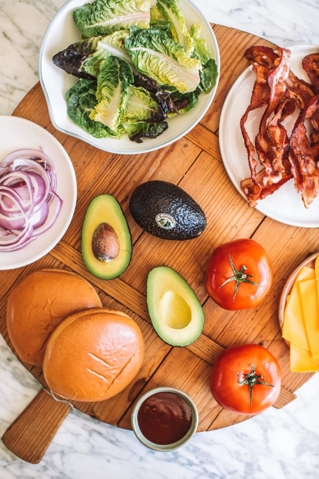 Red onions, lettuce leaves, crispy bacon, brioche buns, halved avocados, tomatoes and cheddar cheese slices.