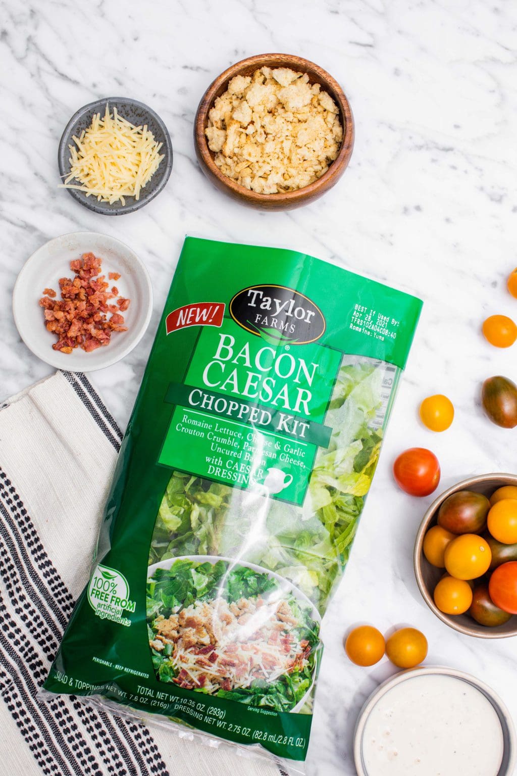 Chopped salad kit with bowls of bacon Parmesan cheese, crouton crumble and cherry tomatoes.