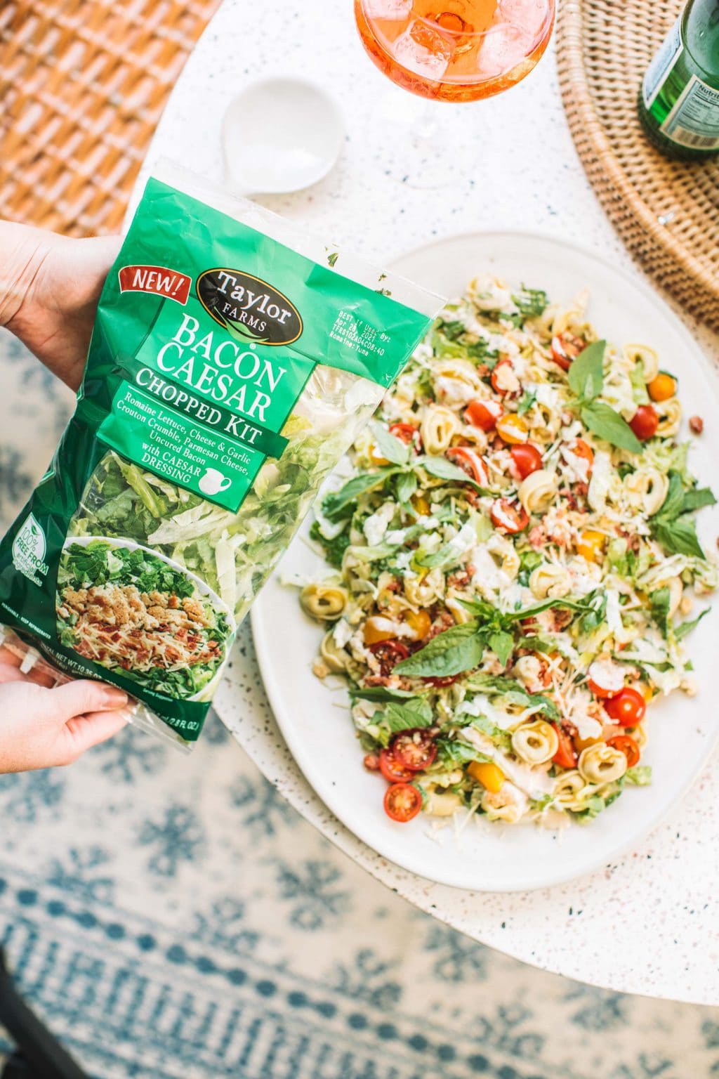 Chopped salad kit bag being held over the table and pasta salad.