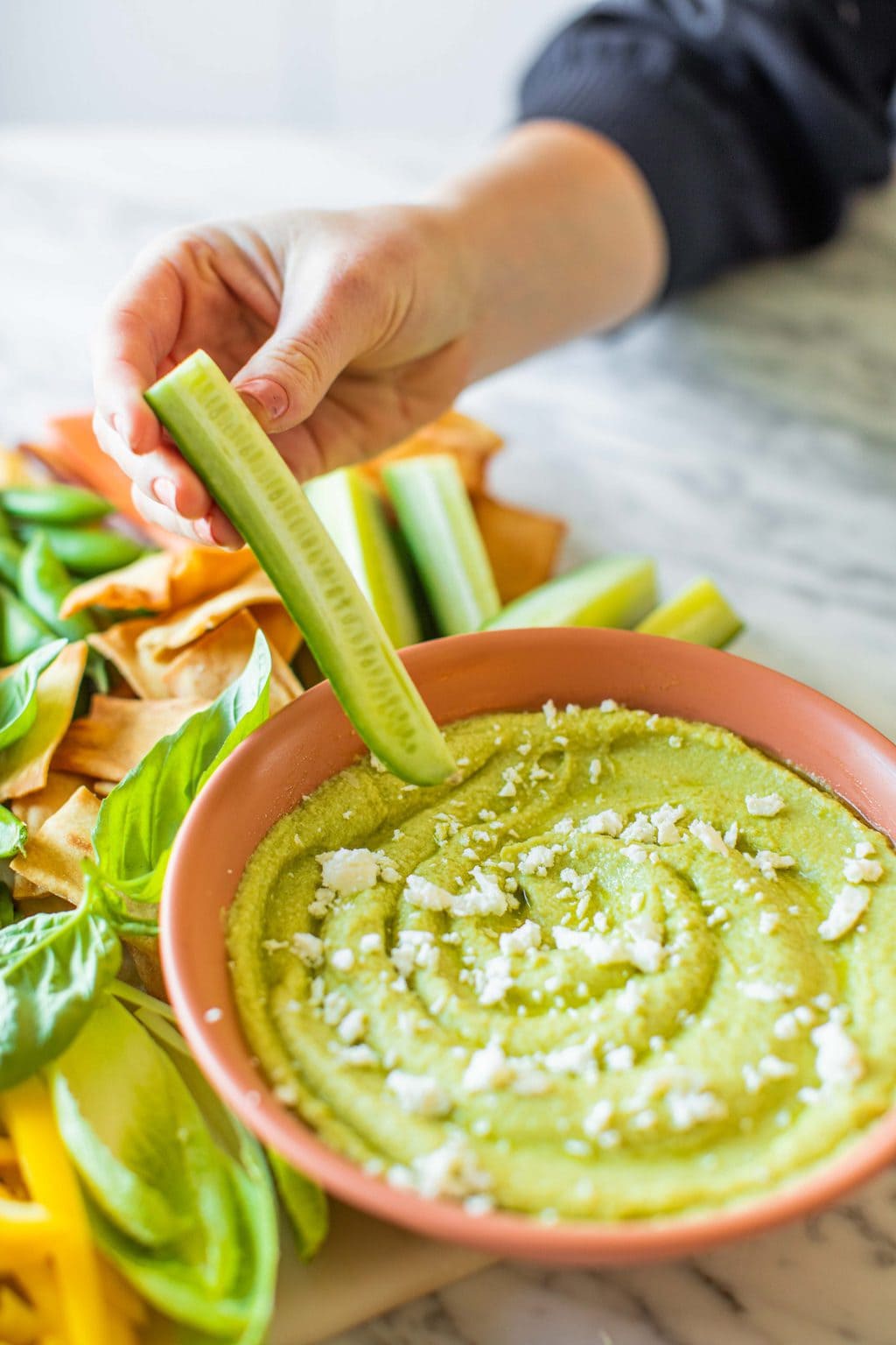 A cucumber spear being dipped into the avocado dip in a pink bowl.