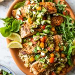 Mediterranean salmon over a bed of couscous and arugula on large orange platter