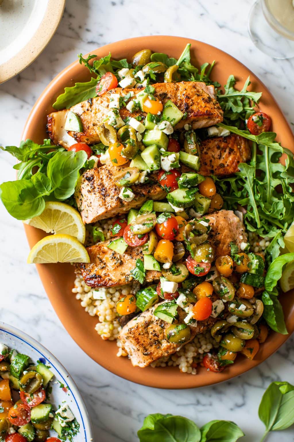 Mediterranean salmon over a bed of couscous and arugula on large orange platter