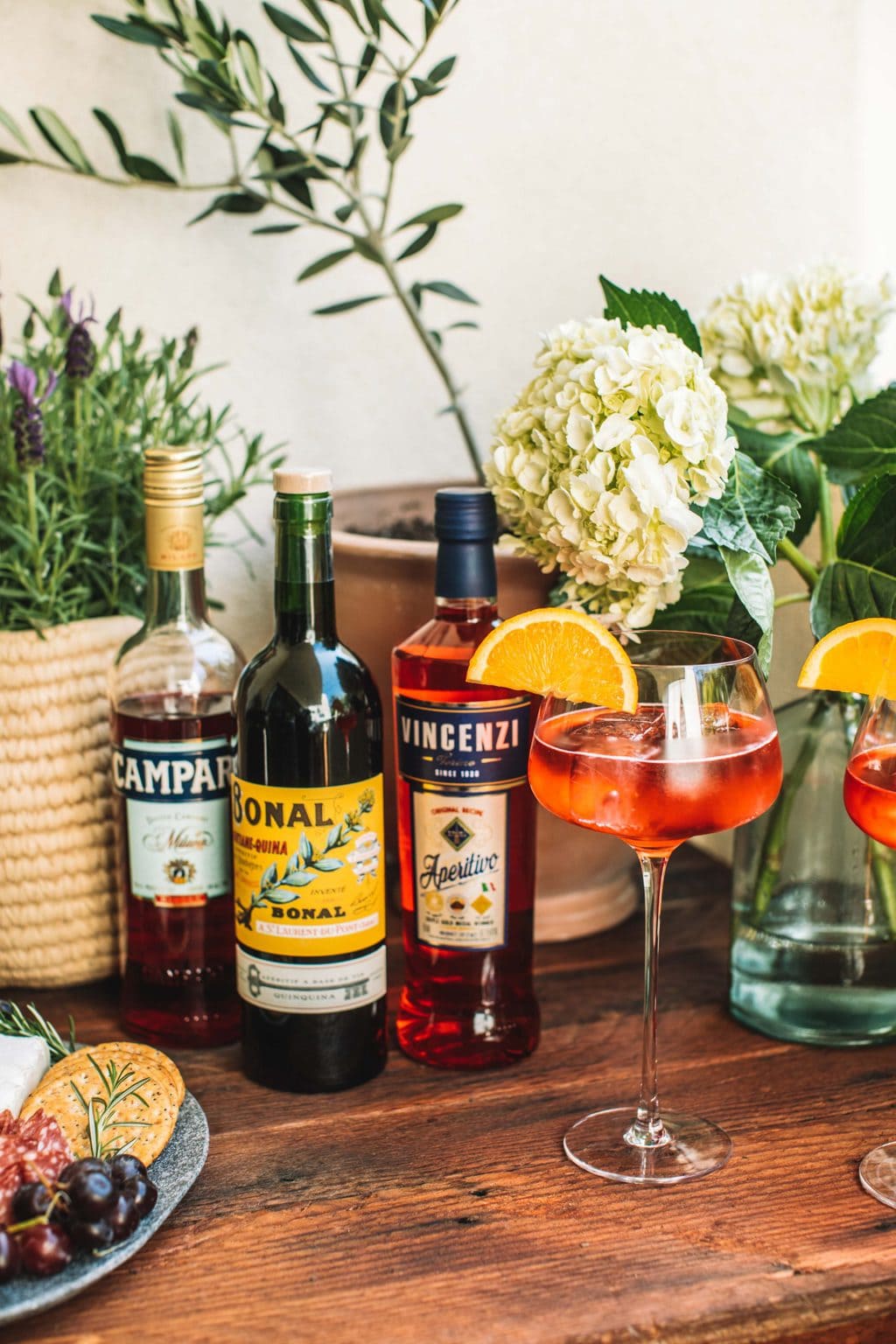 On the wooden pizza table are three different bottles of aperol and a glass made with an aperol spritz. 