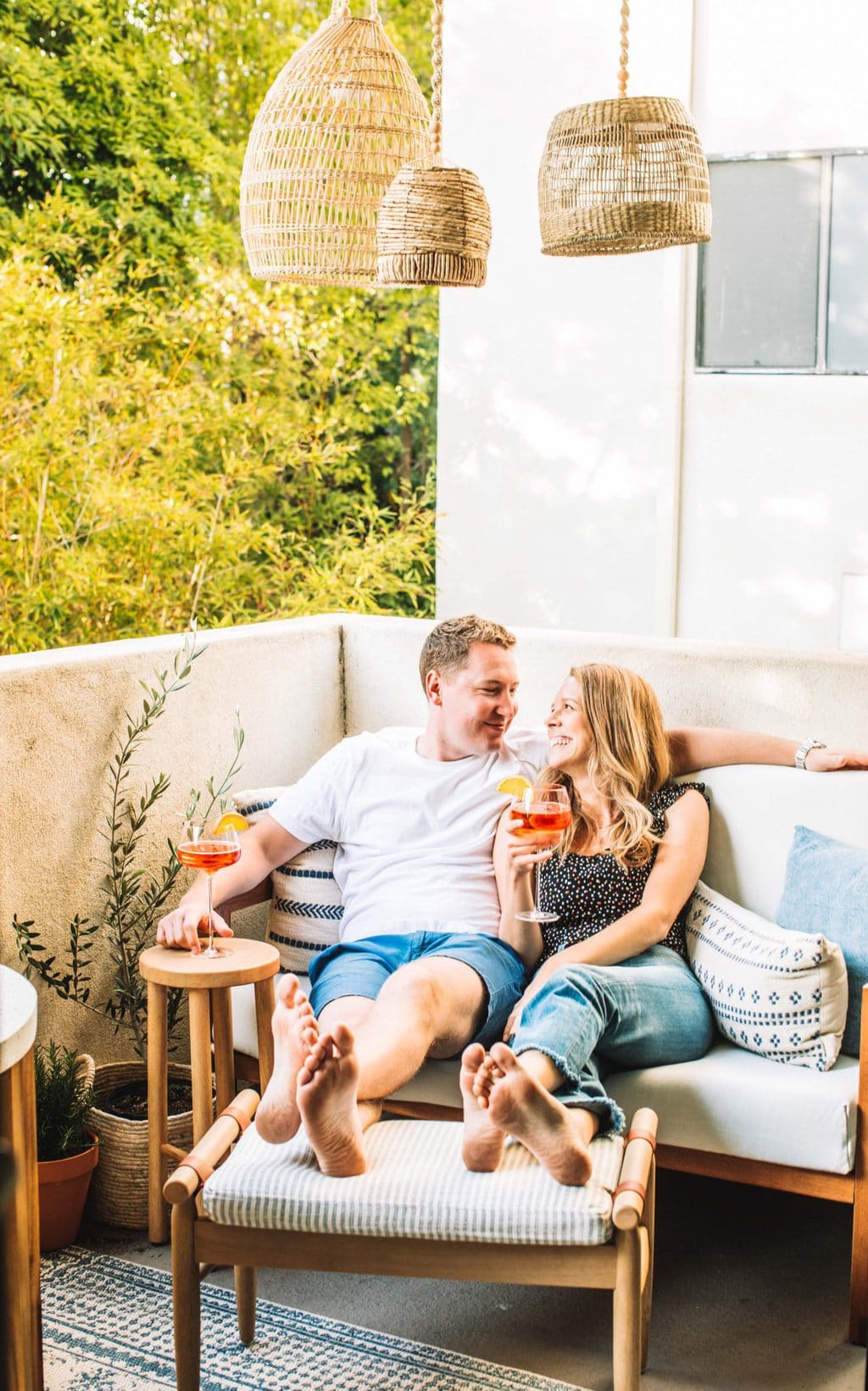 Two people sitting on an outdoor love seat with their feet on a foot stool. 