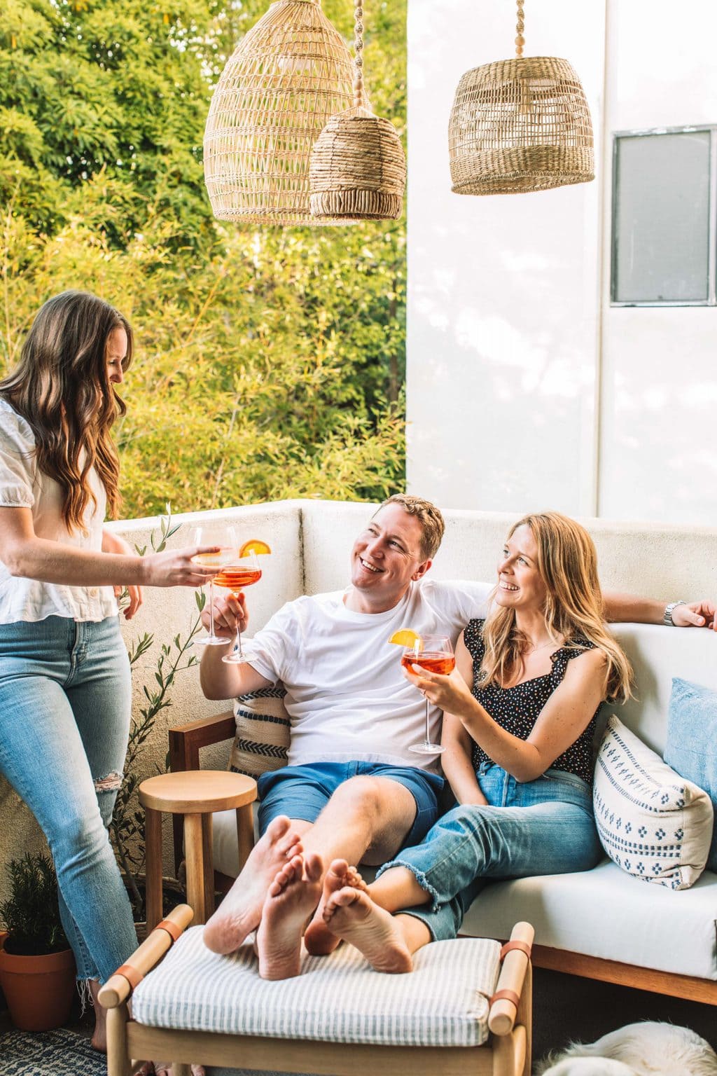 Three people enjoying a lounge space on a love seat and a footstool having a cocktail.