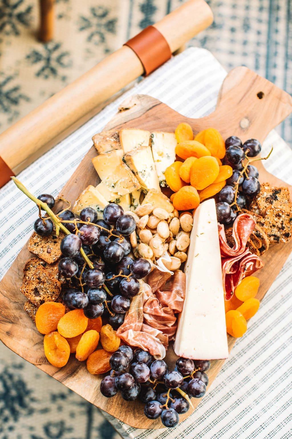 A cheeseboard on a wooden platter sitting on fabric foot stool. 