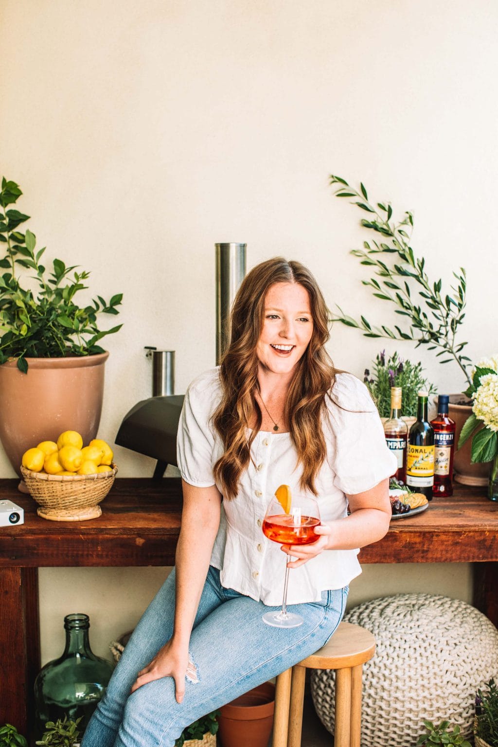 A girl sitting on a stool holding an aperol spritz. 