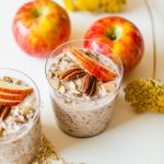 two glasses filled with overnight oats topped with pecans and apple slices
