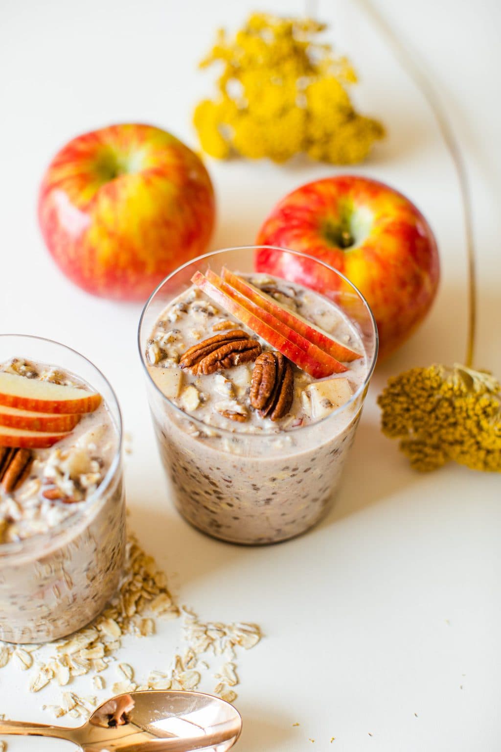 two glasses filled with overnight oats topped with pecans and apple slices