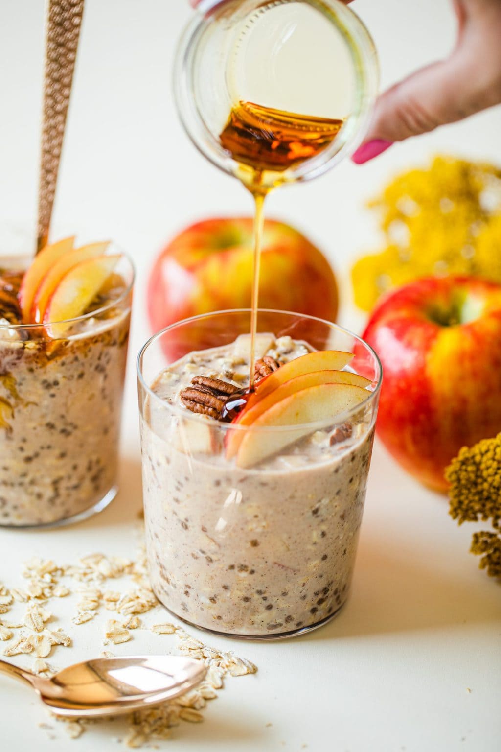 hand pouring maple syrup into glass filled with apple overnight oats