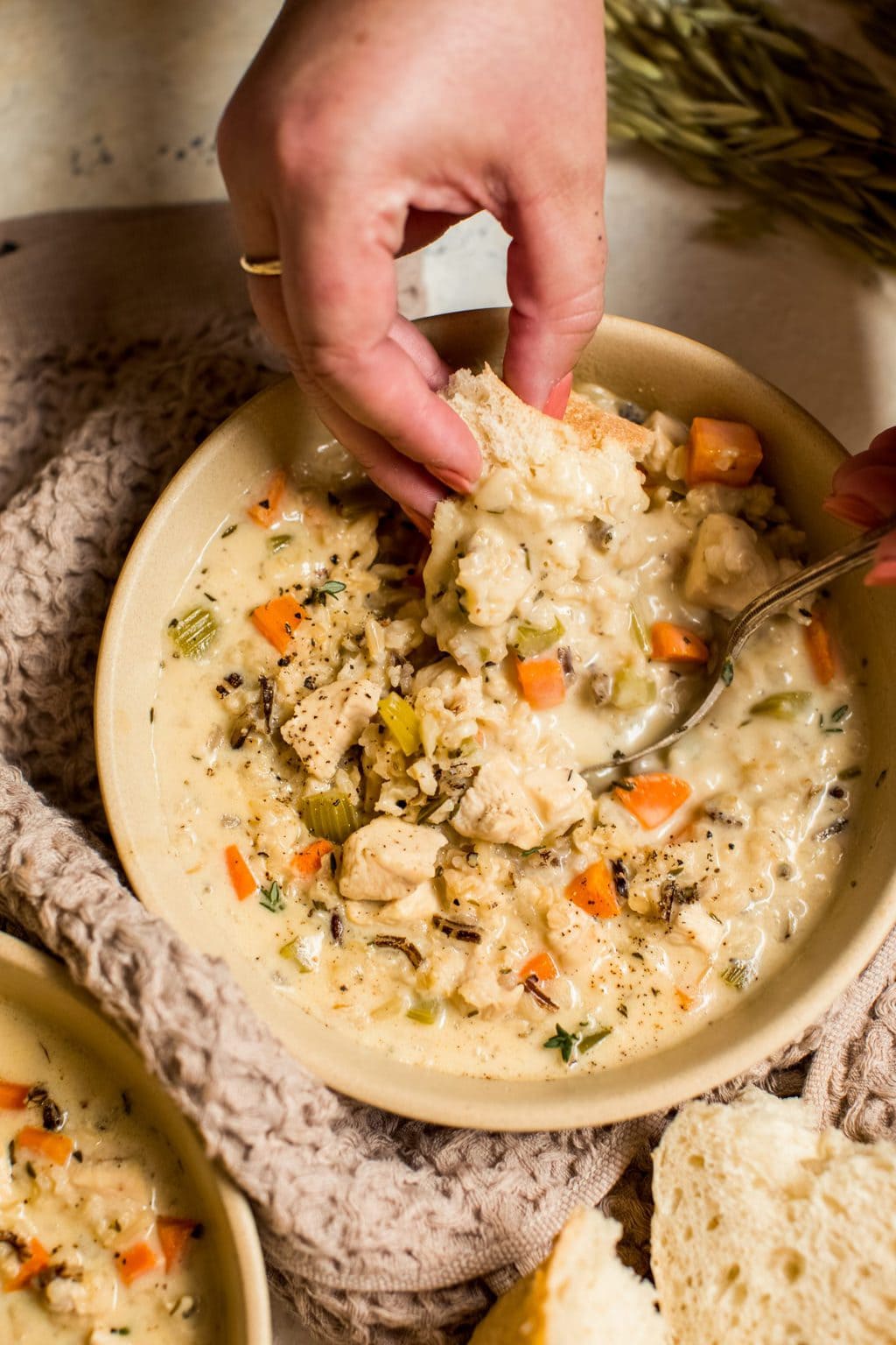 piece of white bread being dipped into creamy chicken and rice soup