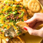 hand scooping cheese ball with cracker