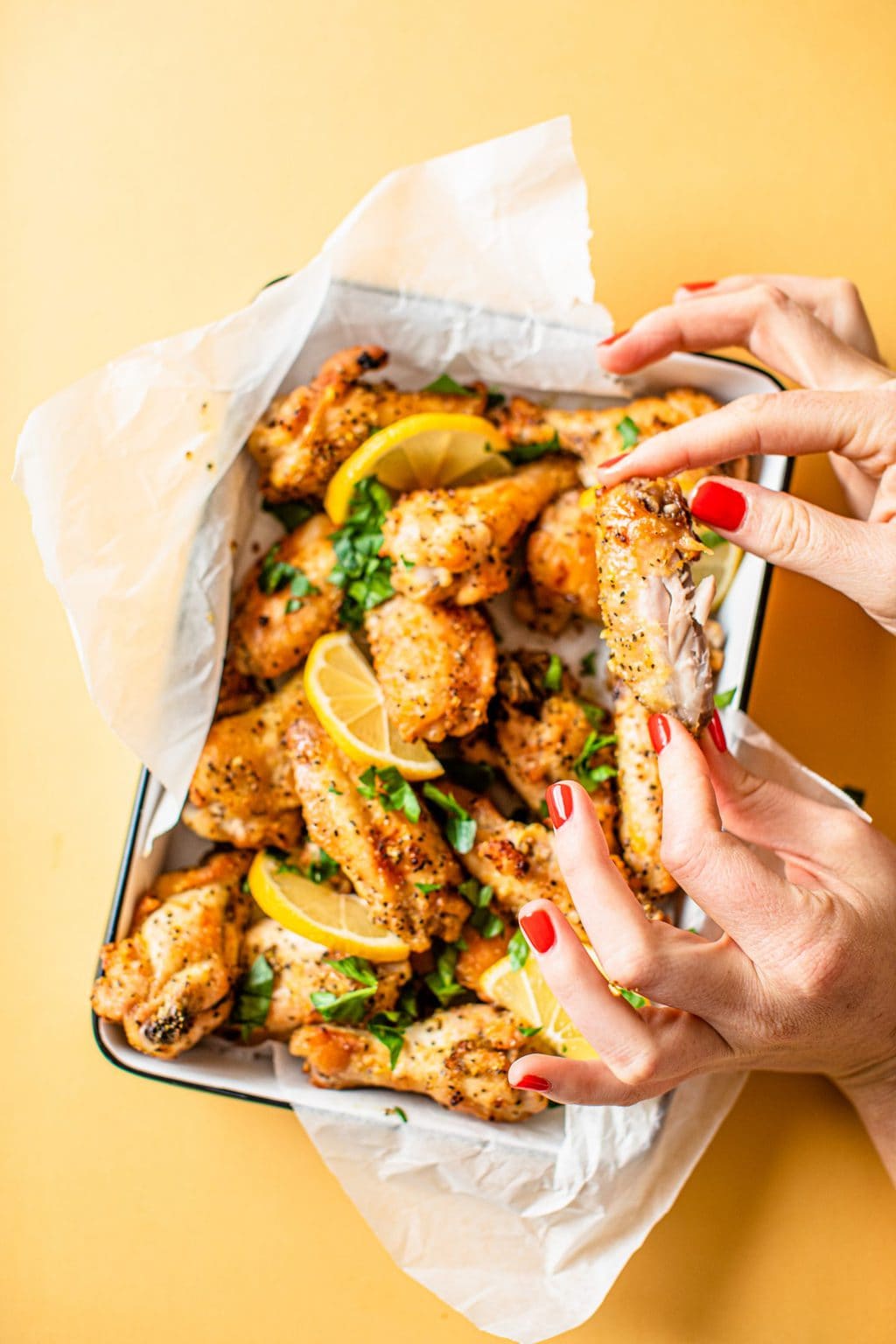 hand holding bitten chicken wing over platter of chicken wings