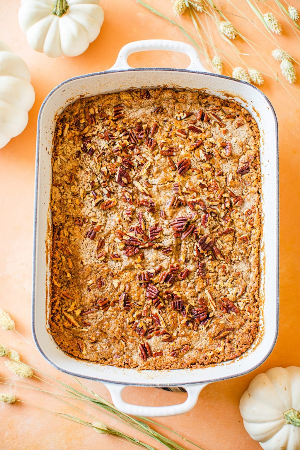 a white casserole dish with pumpkin dump cake and topped with pecans