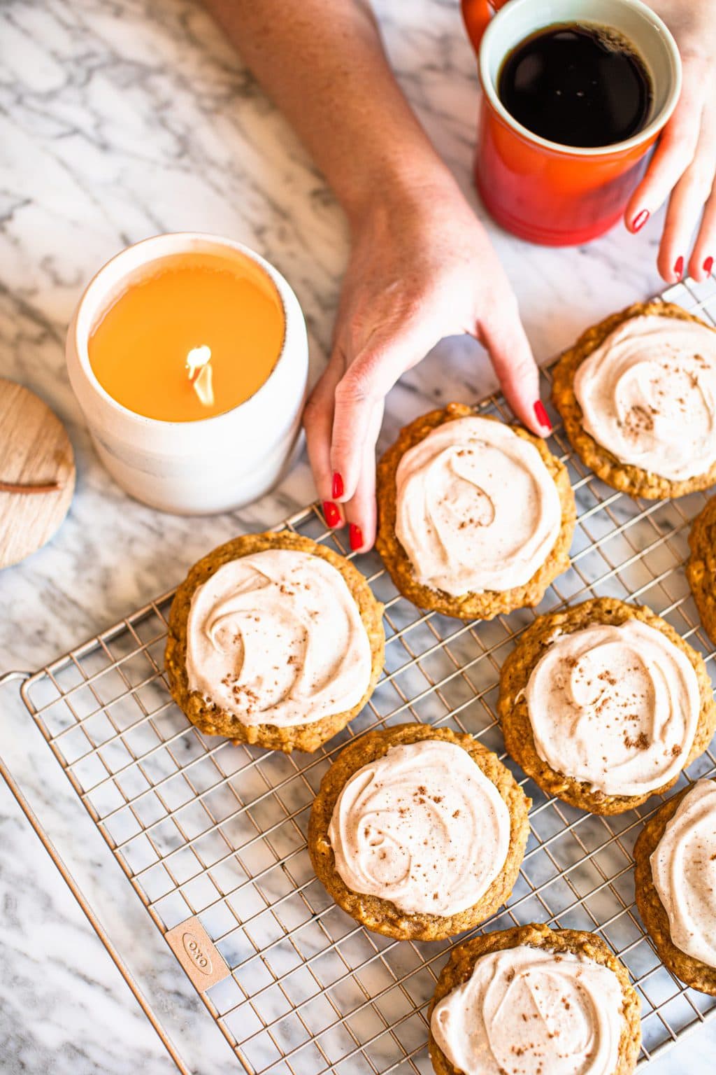 hand grabbing pumpkin oat cookie with icing on cooling rack