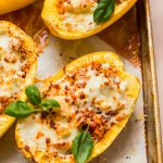 spaghetti squash halves filled with meat, sauce and cheese on baking sheet
