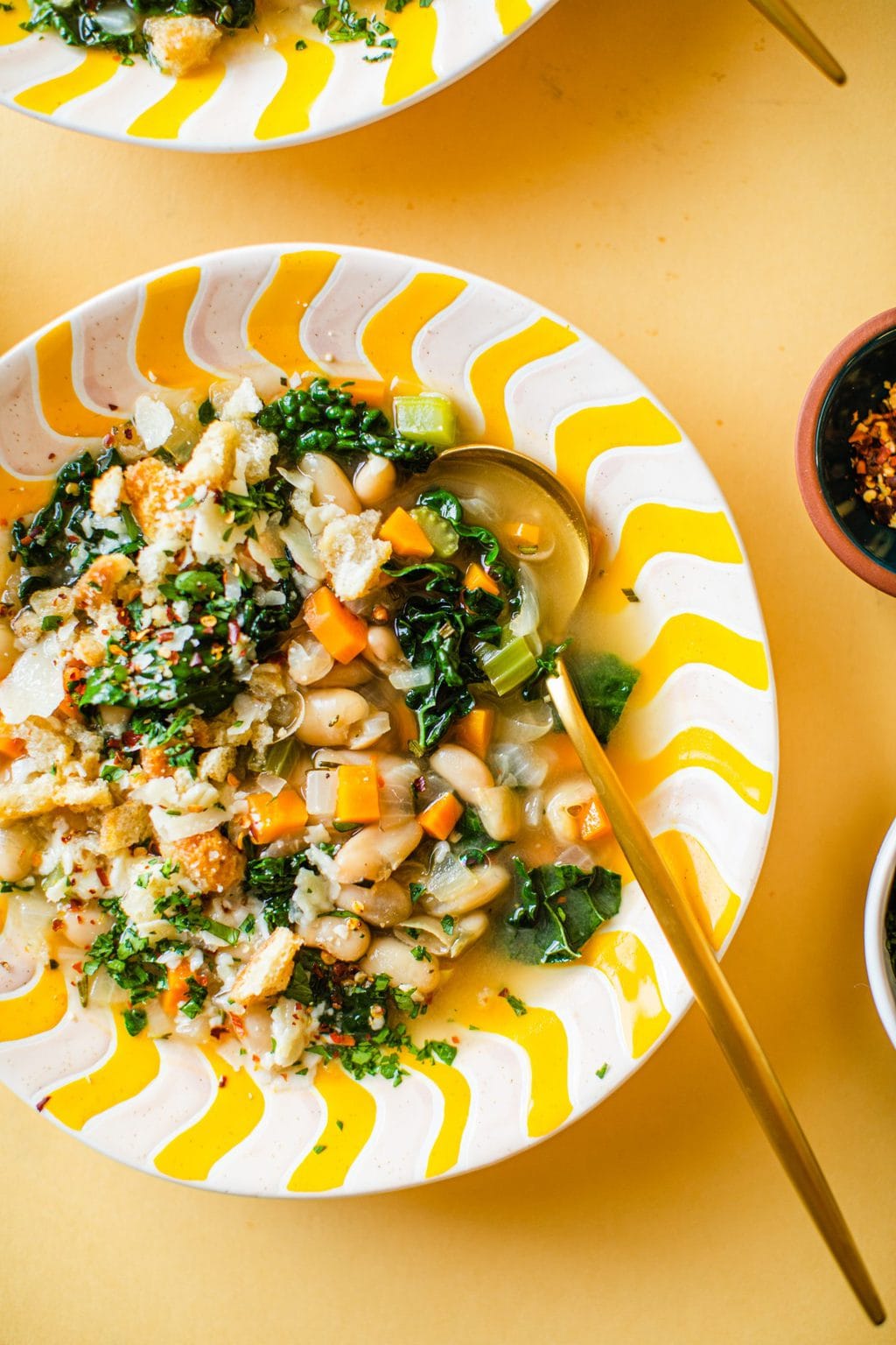 white bean kale soup in yellow and white bowl with gold spoon