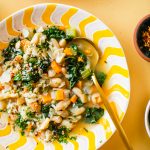 white bean kale soup in yellow and white bowl with gold spoon