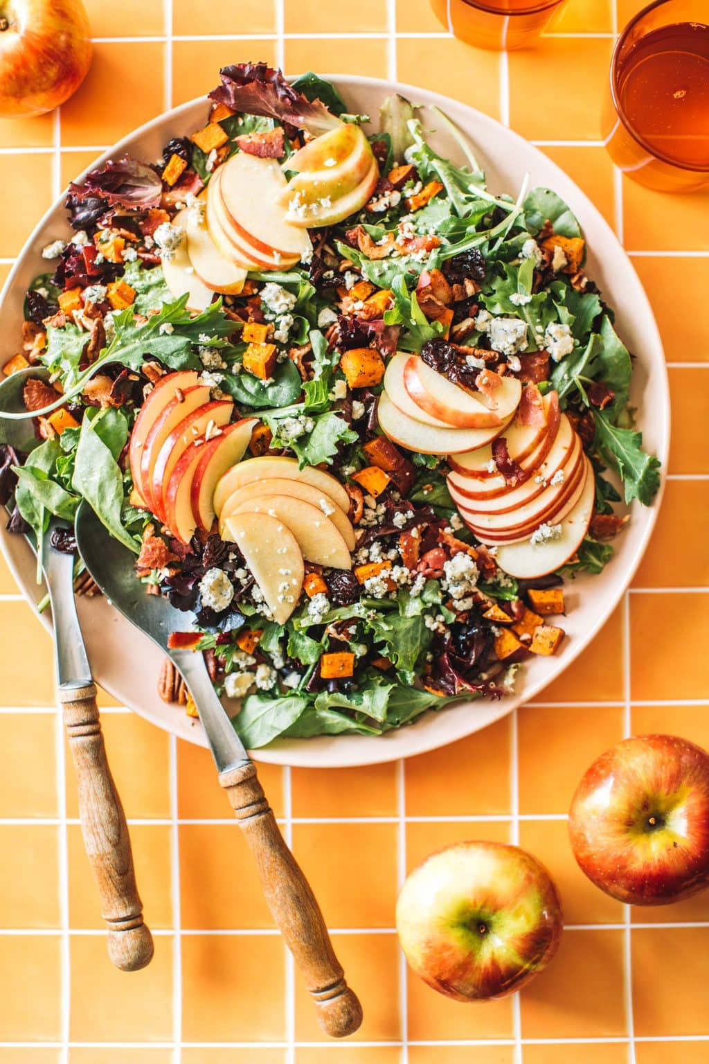 two spoons tossing salad greens, apples, pecans, blue cheese and cranberries in bowl