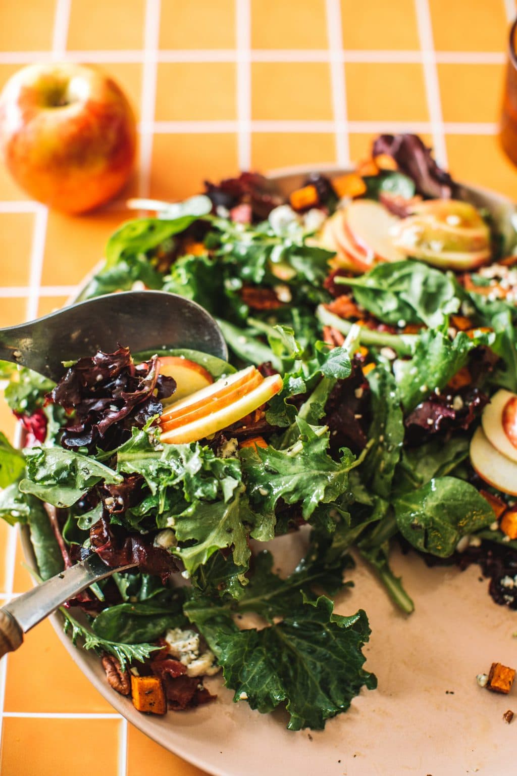 two spoons tossing salad greens, apples, pecans, blue cheese and cranberries in bowl