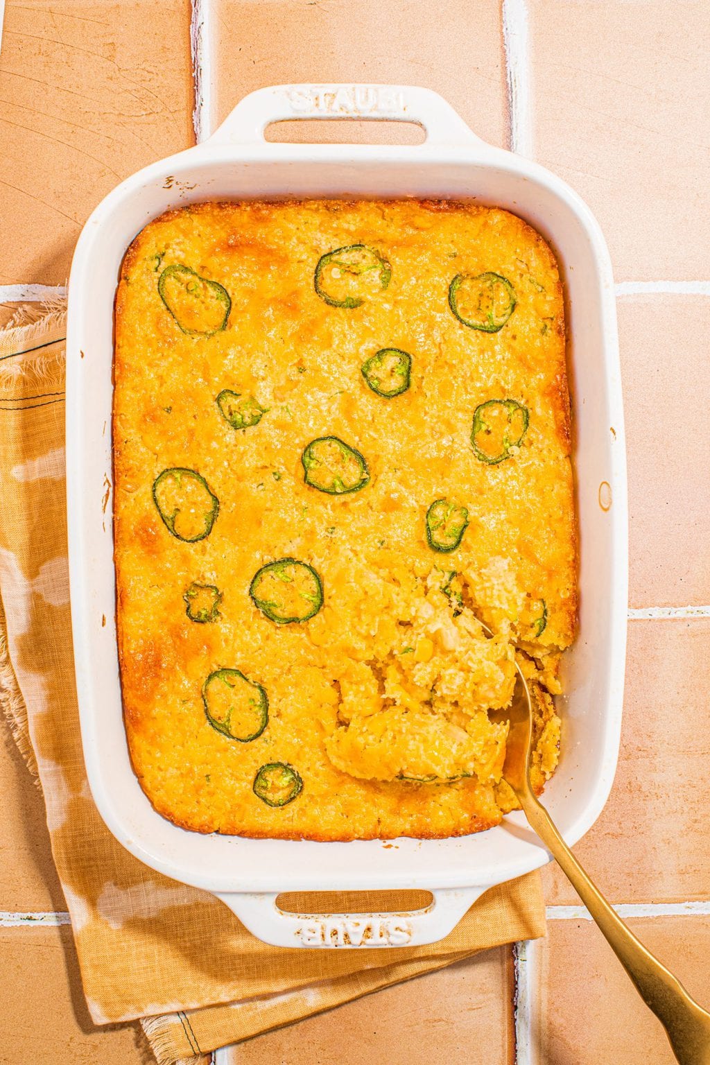 baked cornbread casserole in white casserole dish with serving spoon