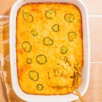 baked cornbread casserole in white casserole dish with serving spoon