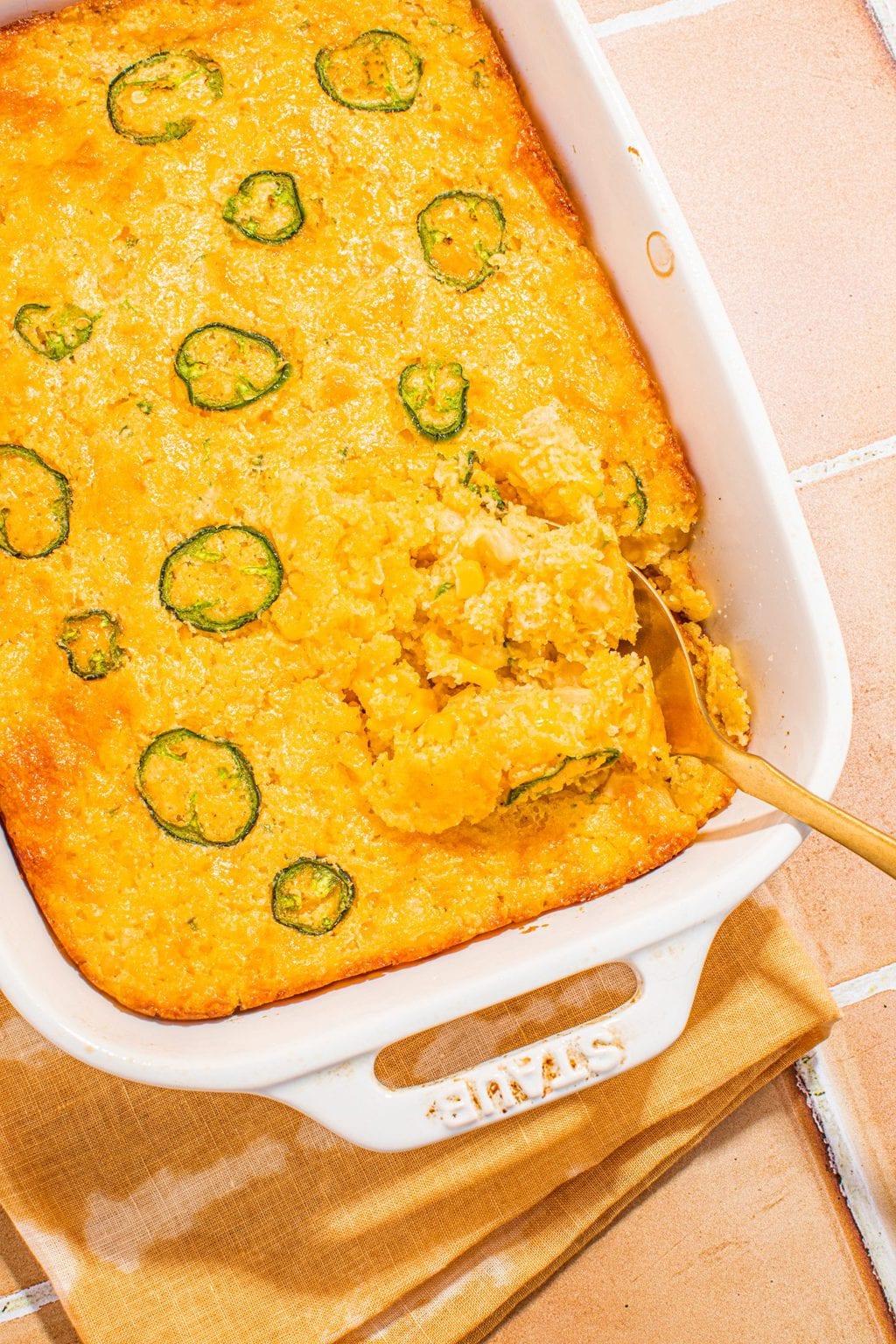 baked cornbread casserole in white casserole dish with serving spoon