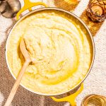 creamy garlic butter mashed potatoes in yellow pot with wooden spoon