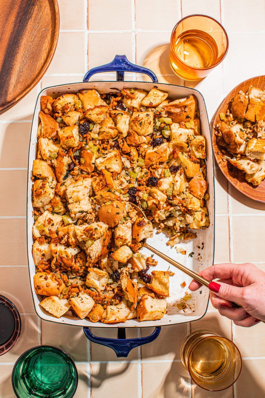 hand scooping out sausage herb stuffing from white baking dish