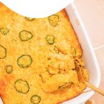 baked cornbread casserole in white casserole dish with serving spoon