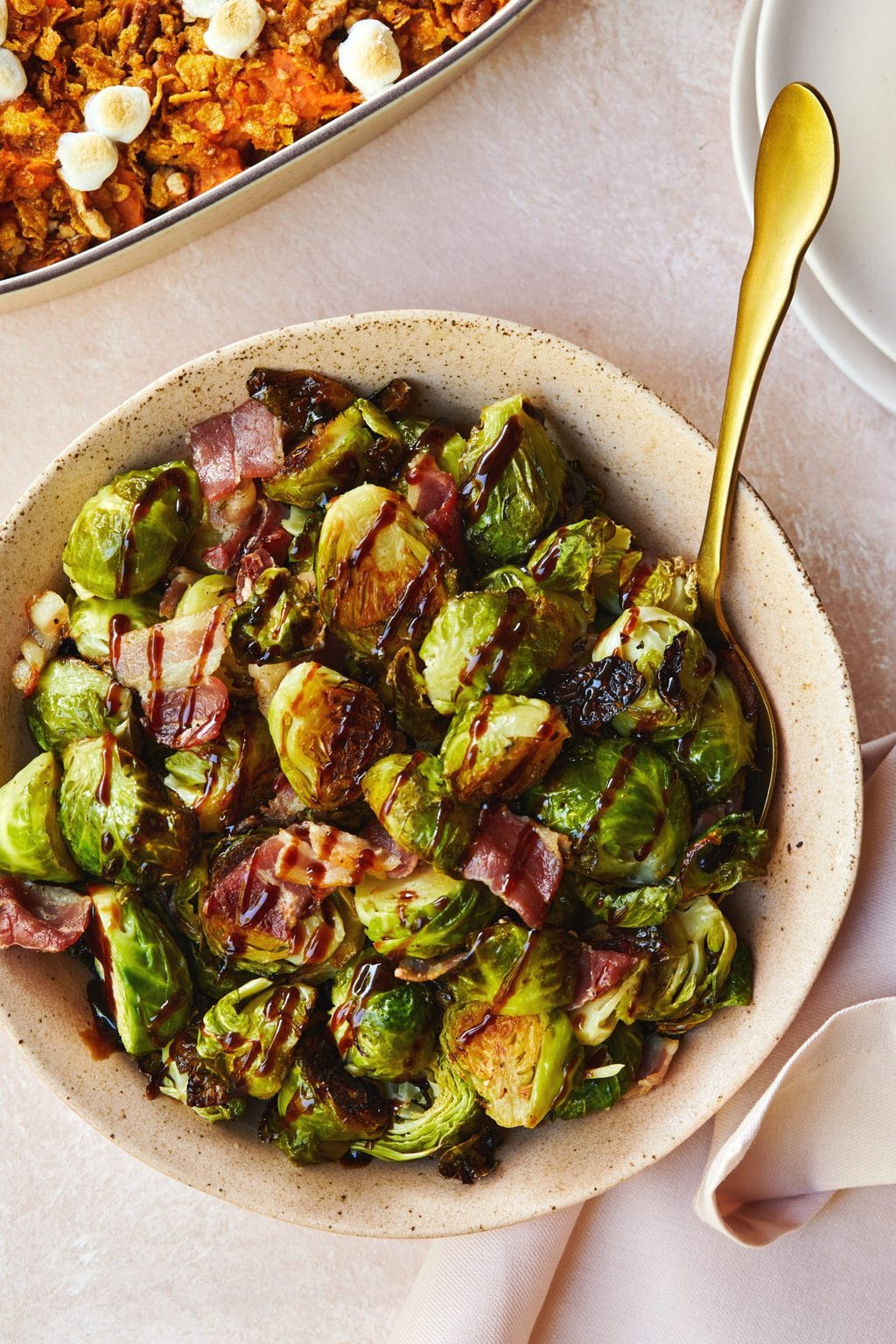 Roasted brussels sprouts served in a pink speckled bowl with a gold serving spoon. 