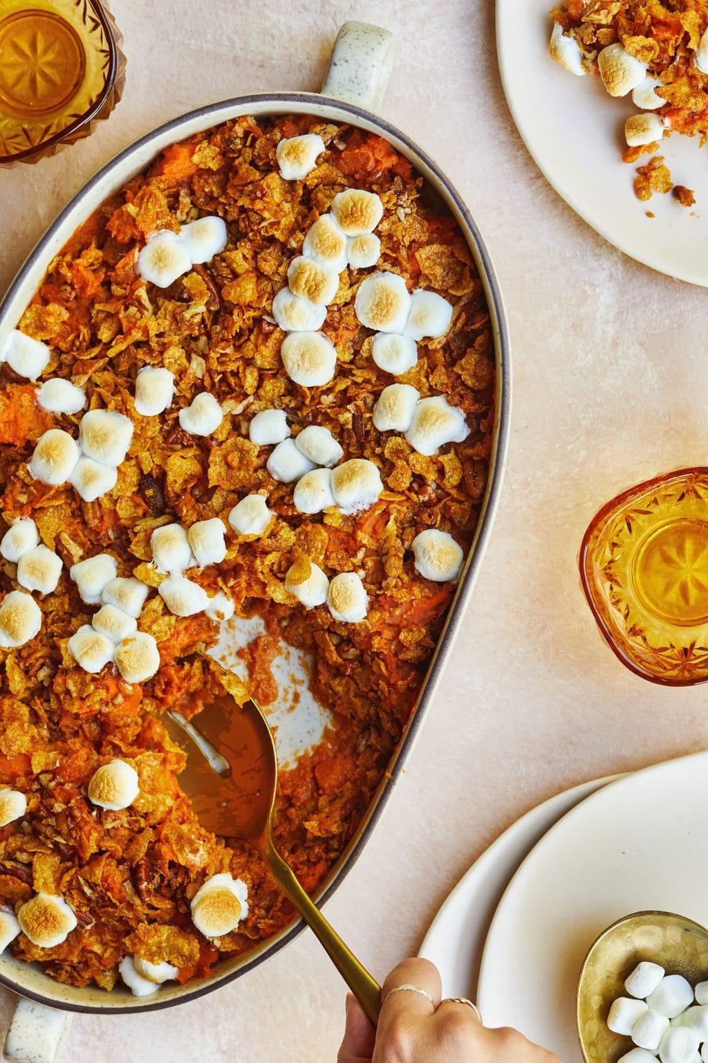 Mashed sweet potatoes with marshmallows on top and a golden spoon in a white casserole dish.