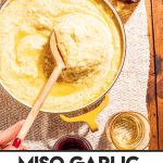 hand scooping spoonful of miso garlic mashed potatoes from yellow pot