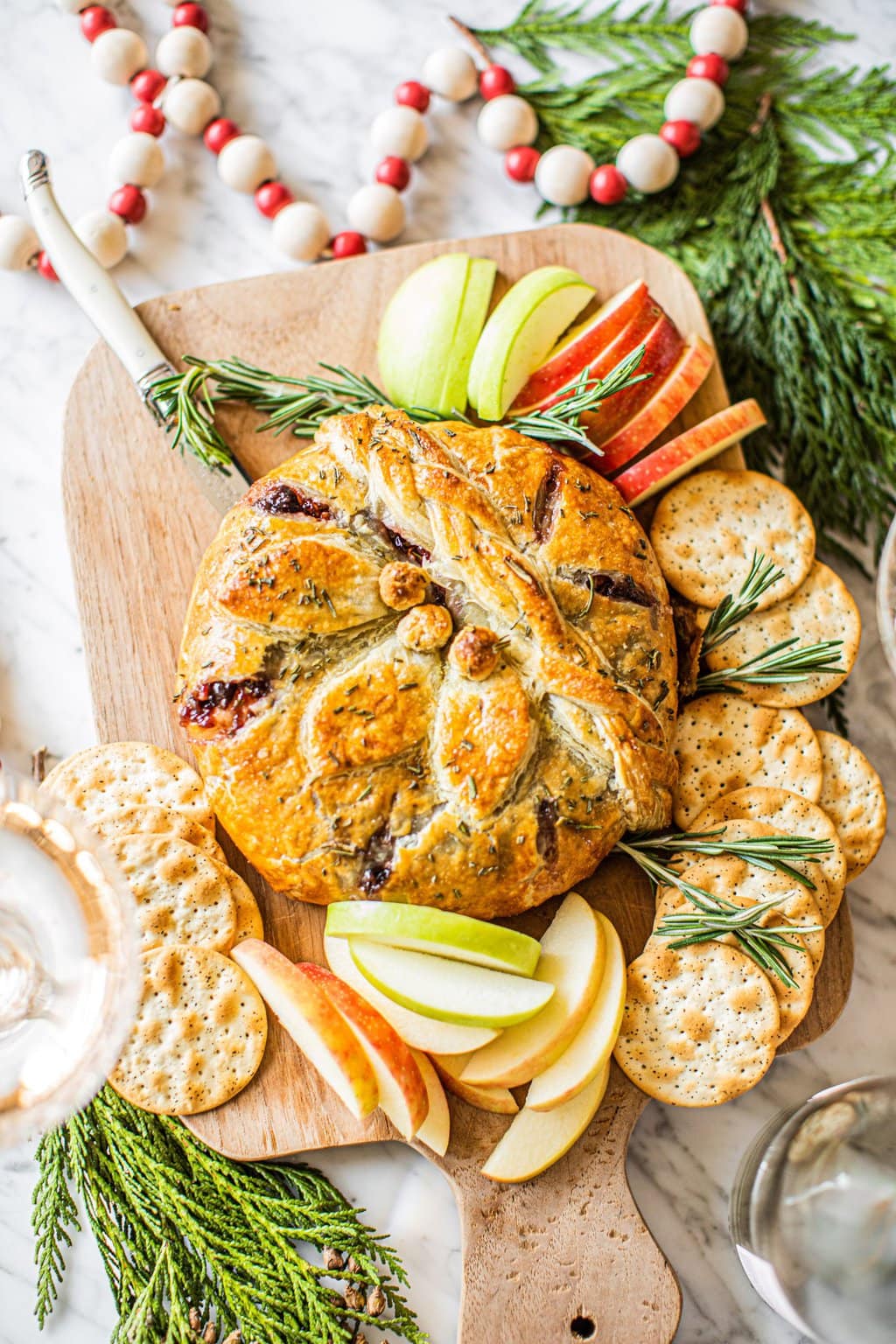 Baked brie on a wooden serving board with apples and crackers. 