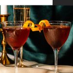 Two chocolate manhattans topped with an orange peel and a luxardo cherry.