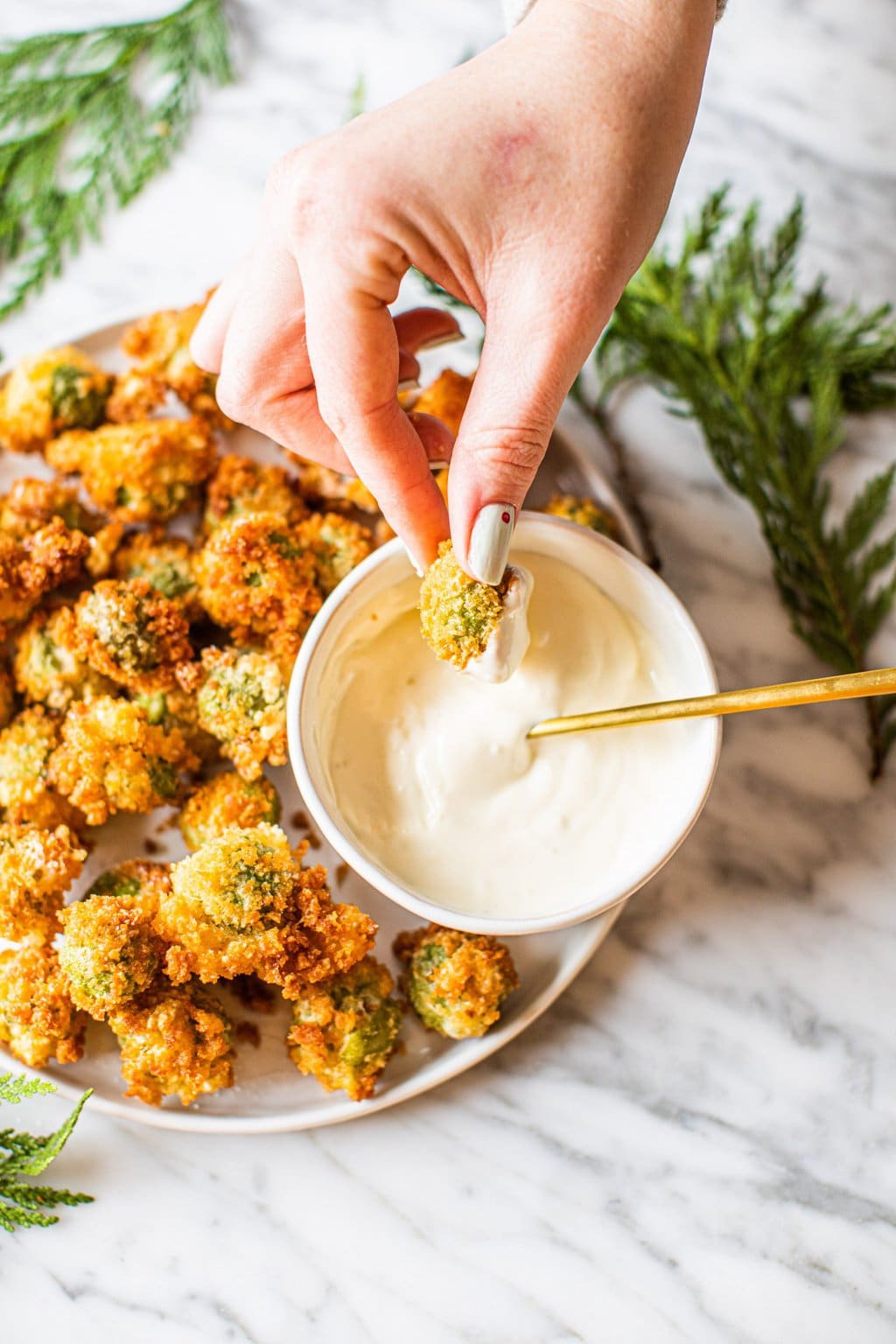 hand dipping fried olive in dipping sauce from platter