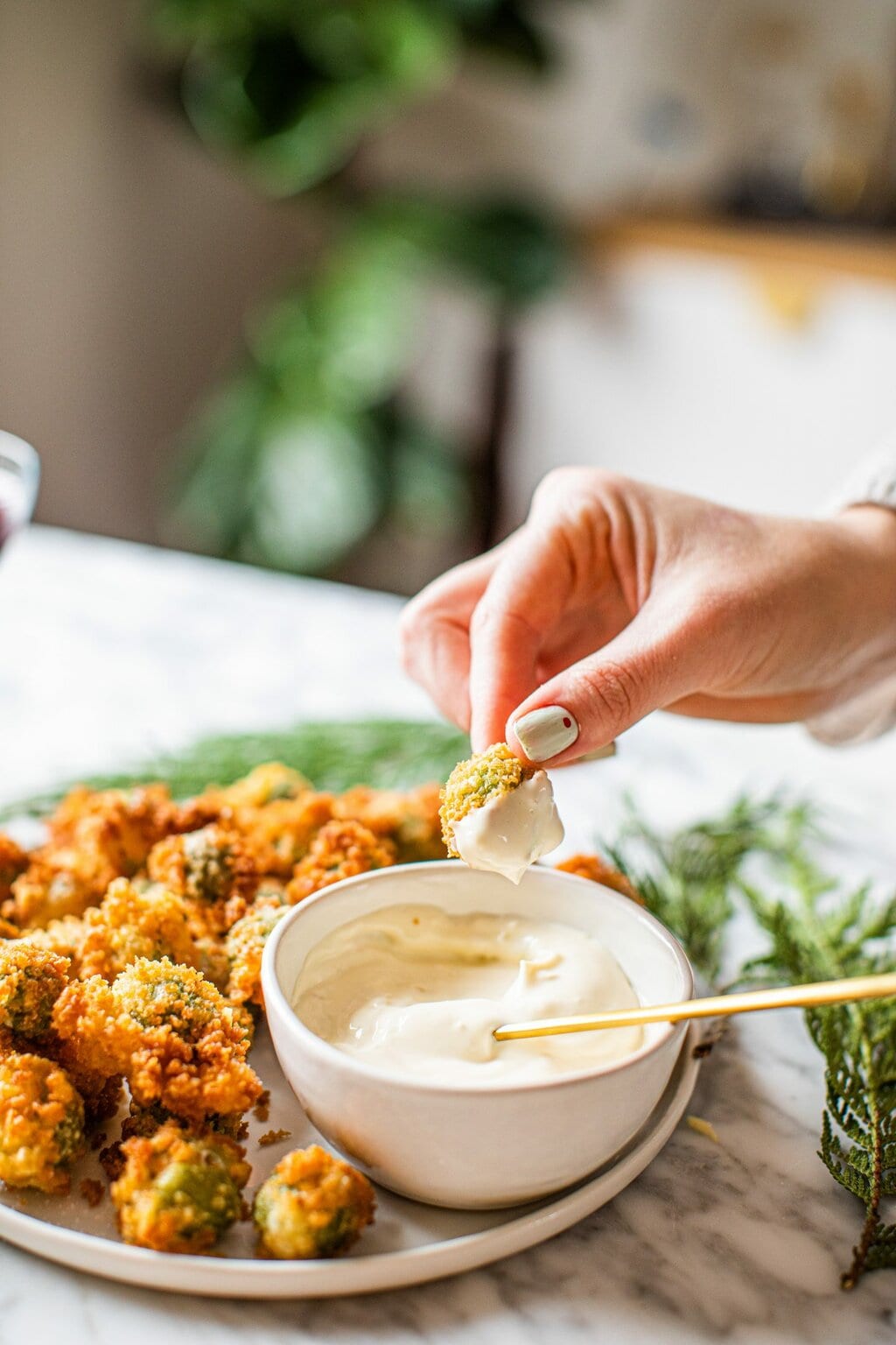 hand dipping fried olive in dipping sauce from platter