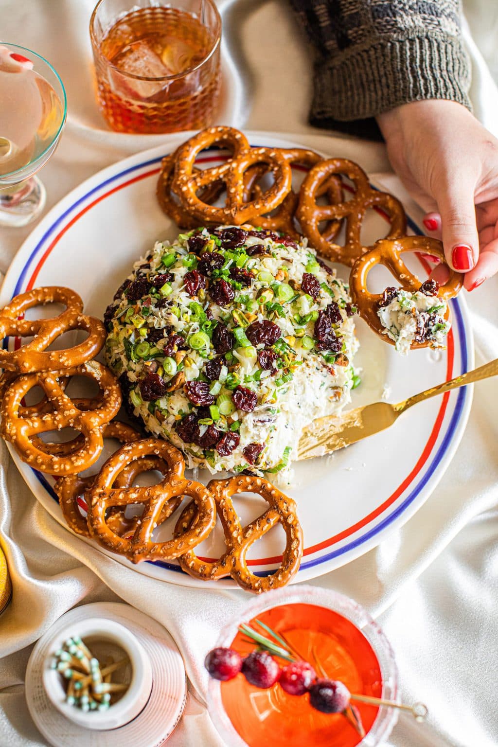 A pretzel being dipped into the cranberry pistachio cheese ball.