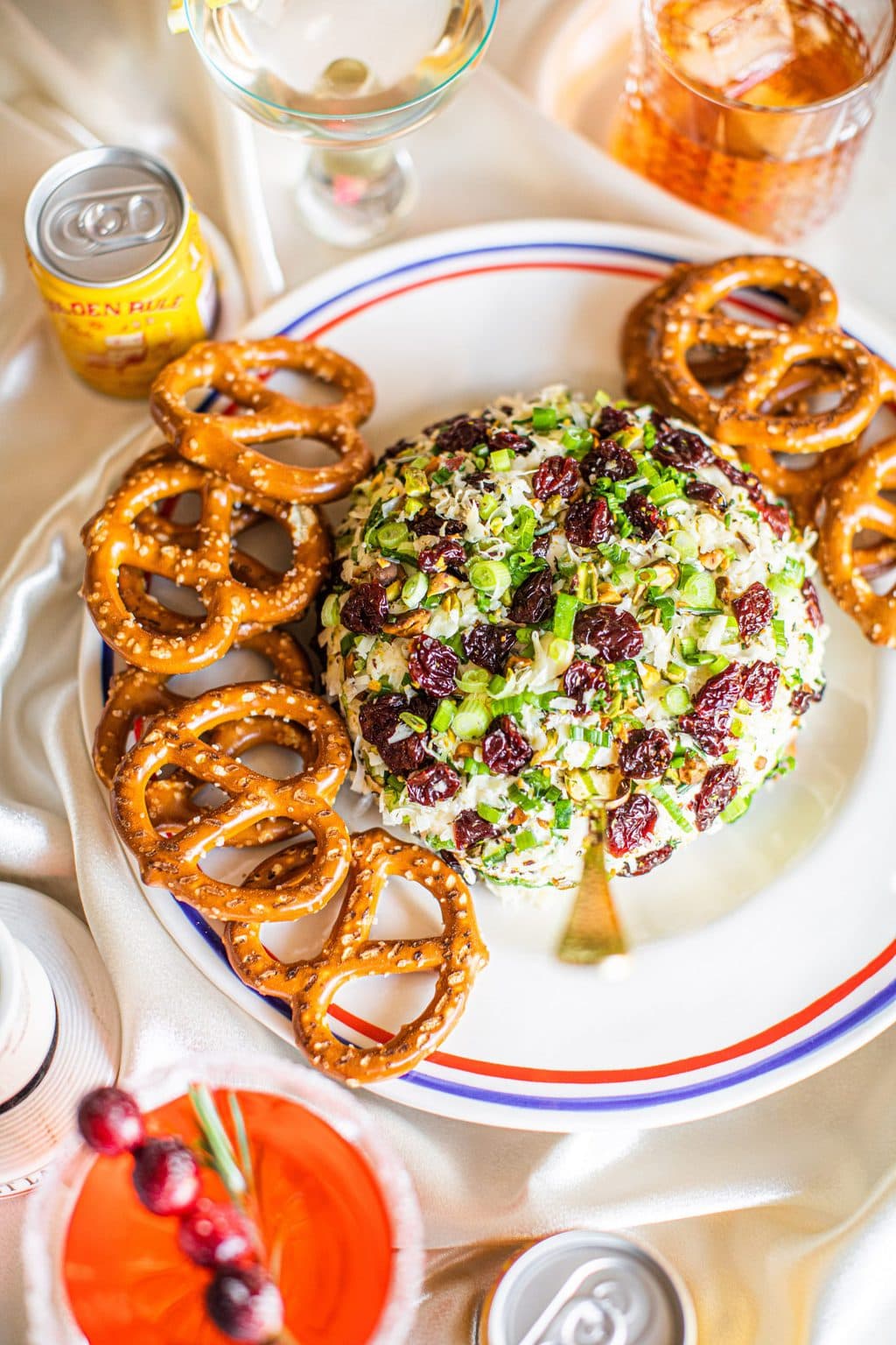 Cheese ball on a white platter with pretzels around it and a cheese spreader in the center of the ball.