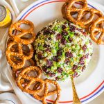 A cheese ball on a white platter with pretzels around it.