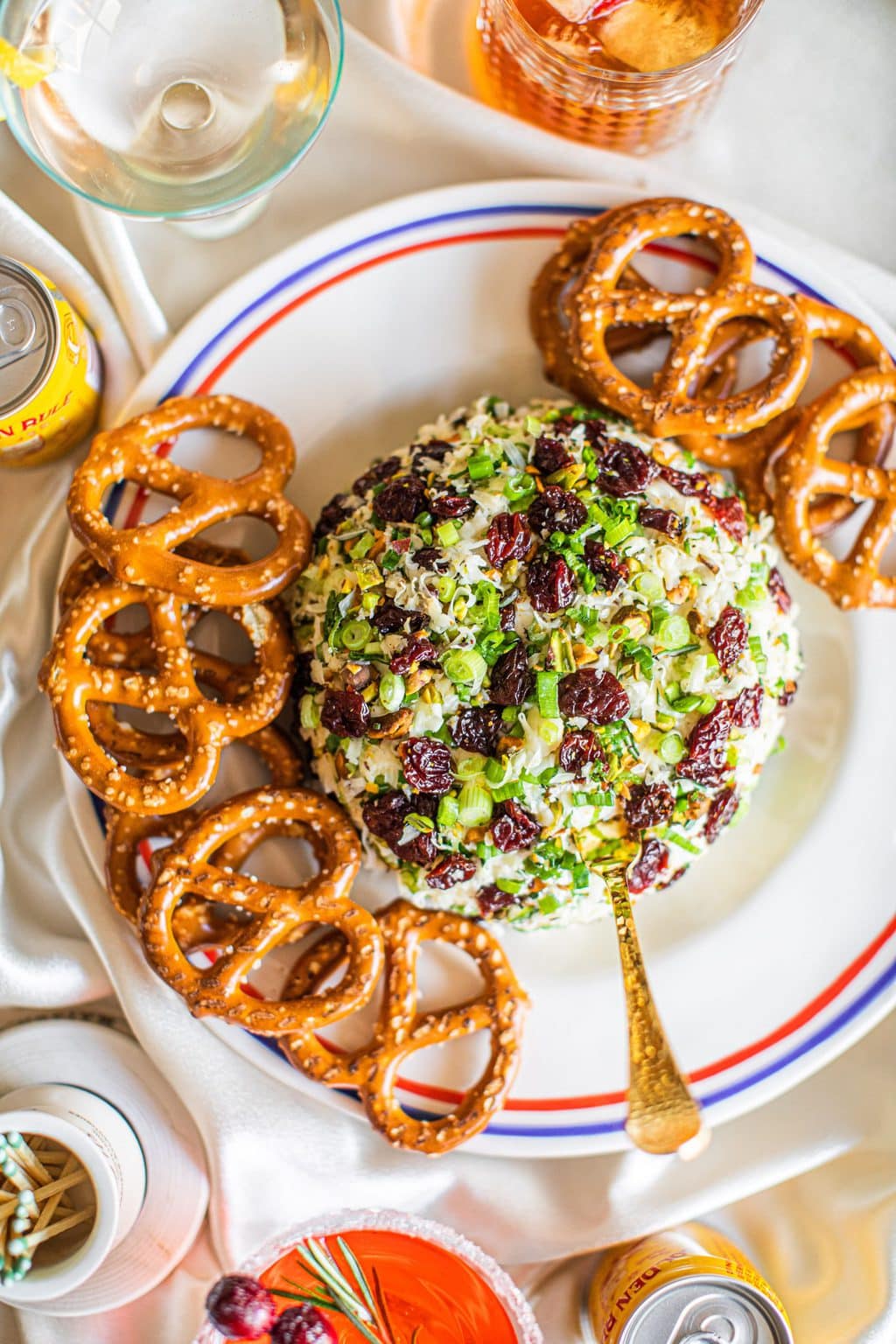 A cheese ball on a white platter with pretzels around it.