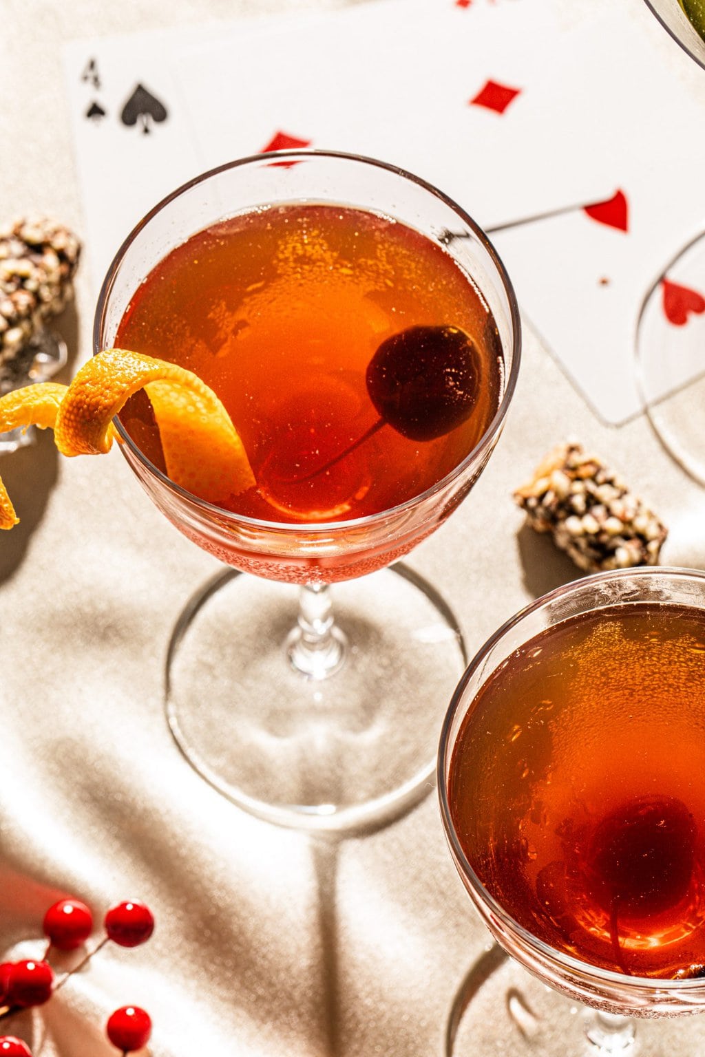 Chocolate manhattan in a coupe glass garnish with an orange peel and a luxardo cherry with playing card surrounding the drink.