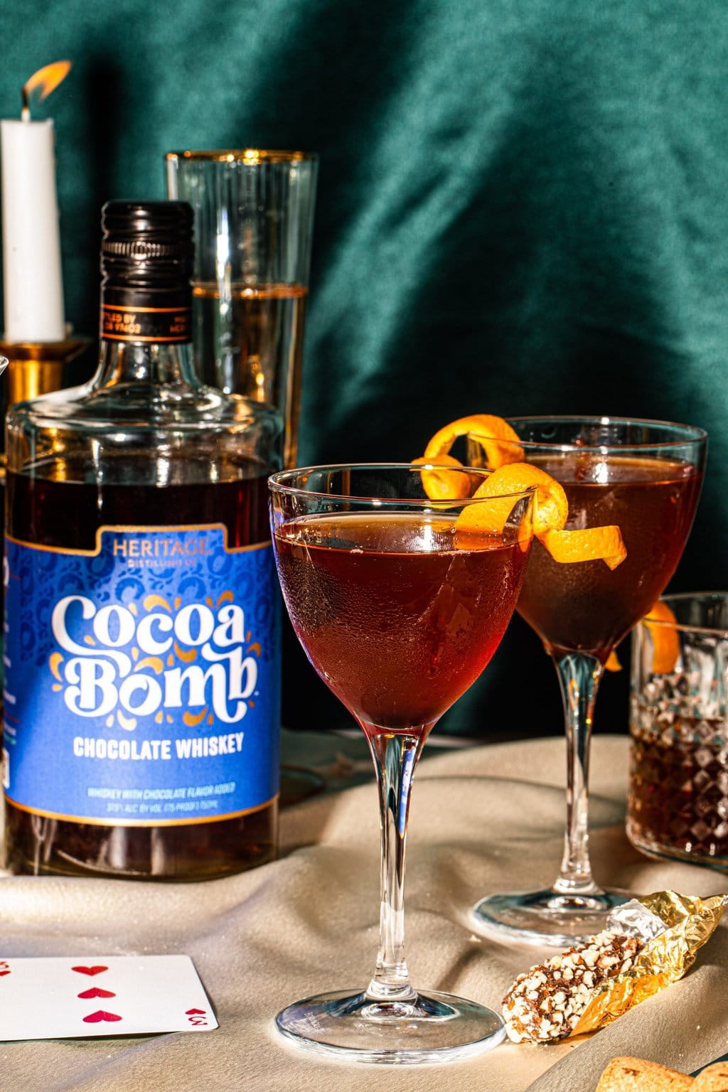 Chocolate manhattan in a small coupe glass next to a cocoa bomb whiskey bottle.