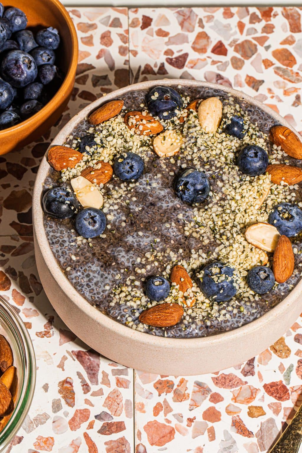 blueberry chia seed pudding in bowl topped with berries, hemp seeds and nuts