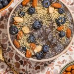 blueberry pudding in bowl topped with berries, hemp seeds and nuts