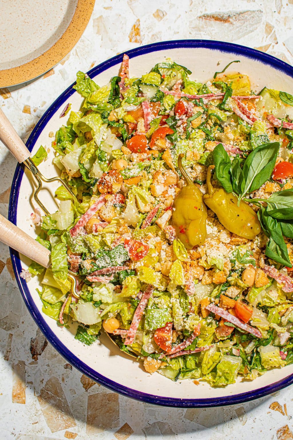 Italian chopped salad in large bowl with serving utensils