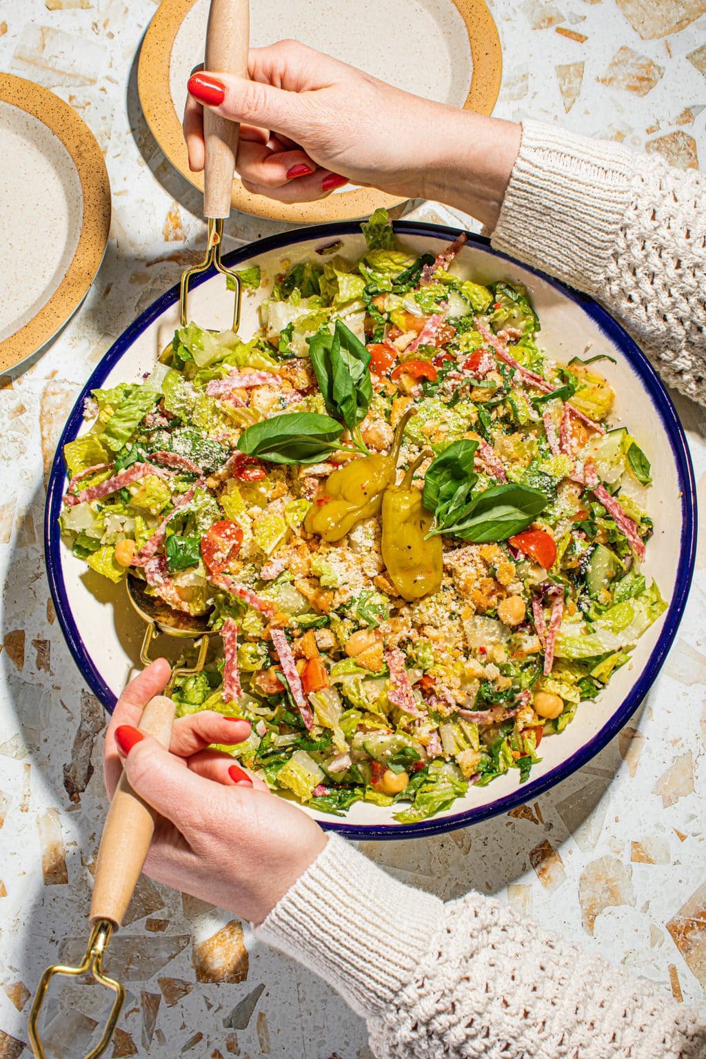 hand tossing chopped salad in large bowl with fork