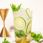 mocktail mojito in highball glass with lime wheels, mint sprig and jigger on side